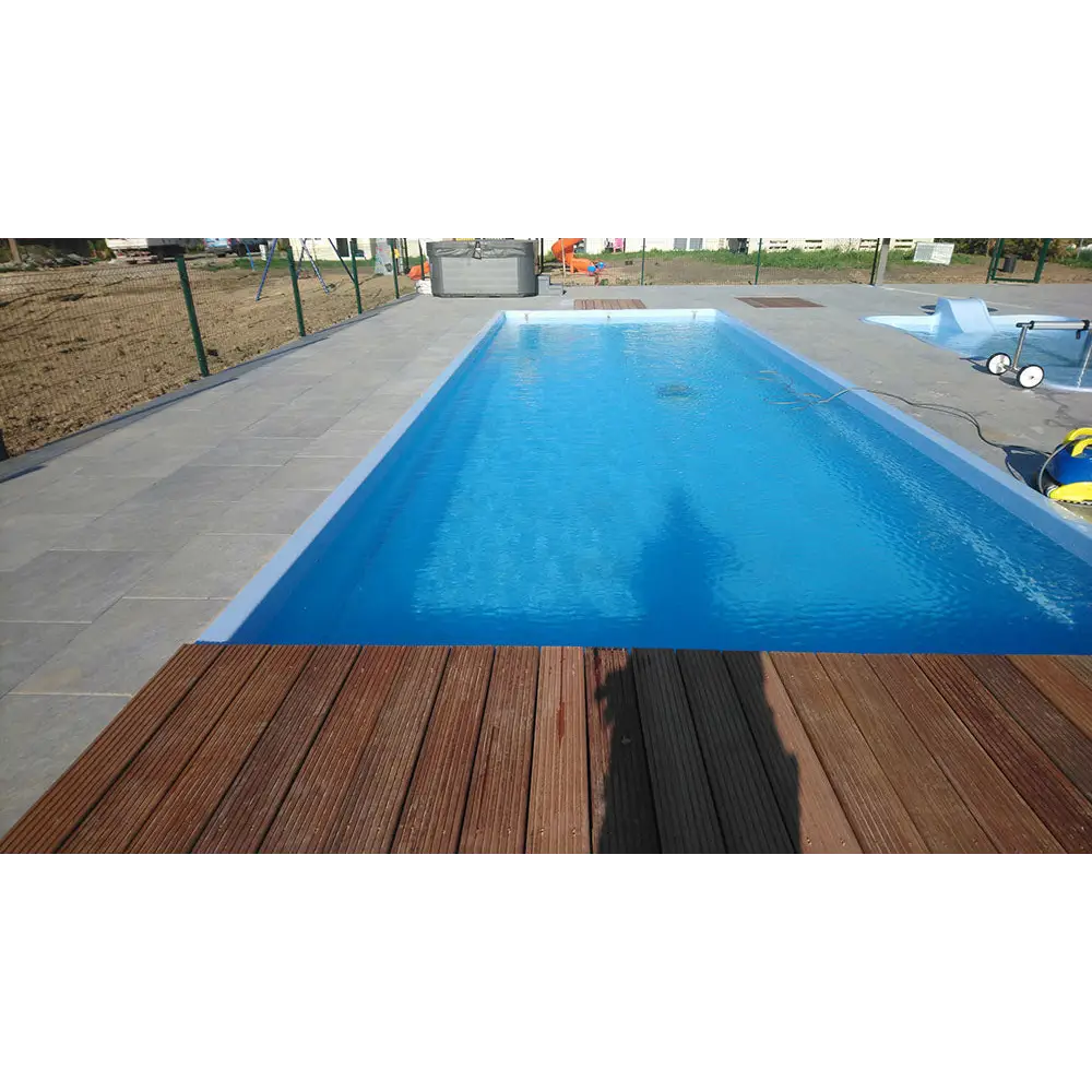 Glasfiberpool Bahama 11 med klarblått vatten och vit insats, grå stenplattor och brun trädeck