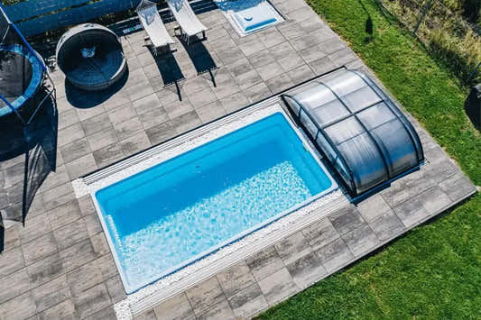 Papeete-glasfiberpool – klart blåt vand, transparent overdækning, grå stenfliser