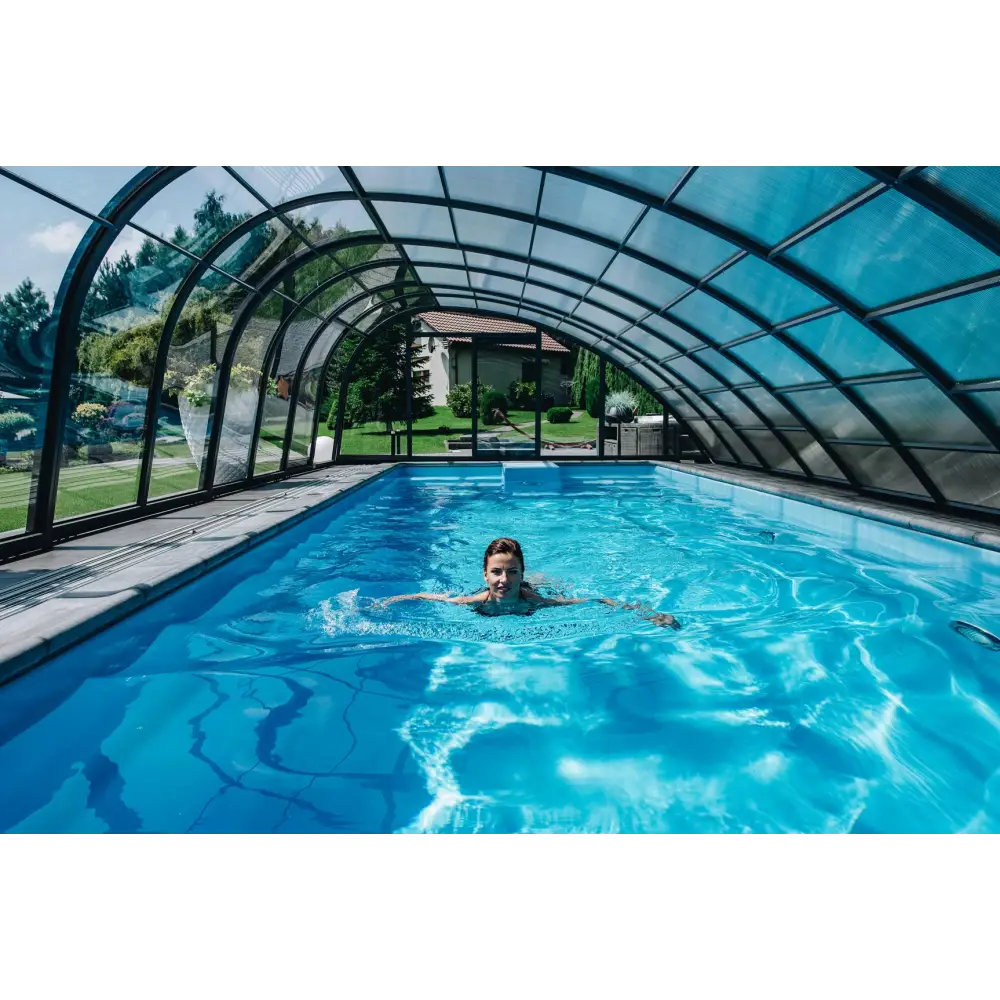 Kvinna simmar i klarblå Glasfiberpool Trinidad 9,70m x 3,70m x 1,60m under valvformad glastak