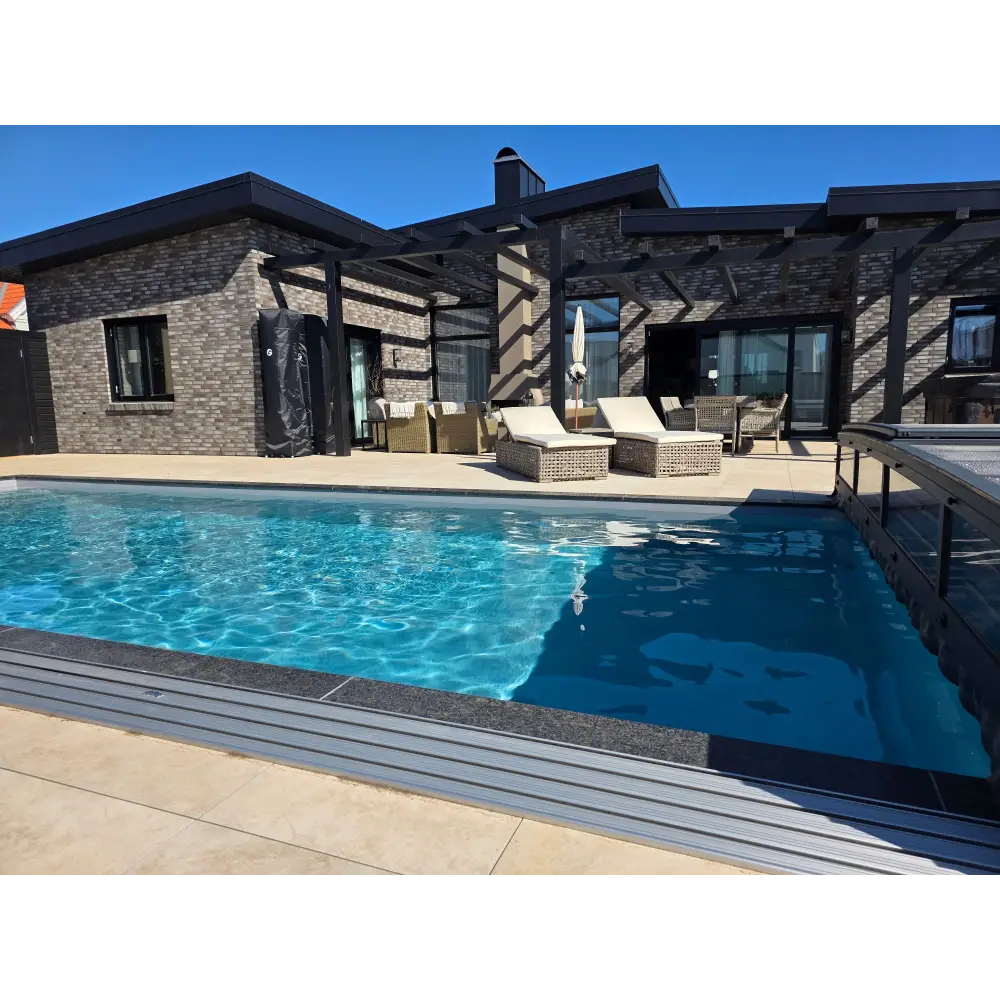 Rektangulär poolpool med klarblått vatten och mörkgrå kakelkanter framför ett modernt stenhustak köp pool