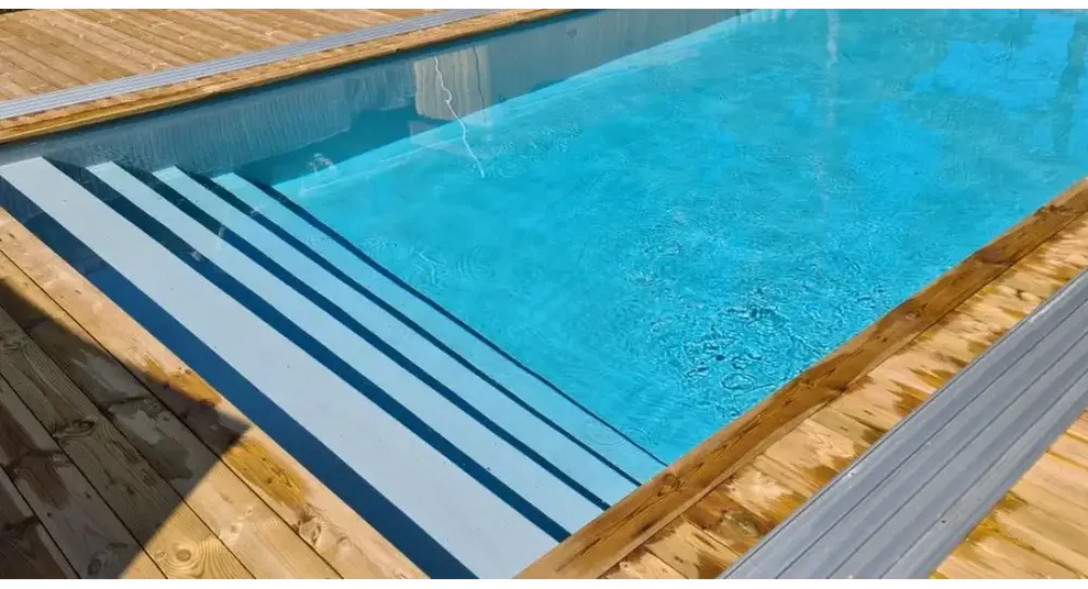 Pooltime Exklusiv 12mm rektangulär pool med klart blått vatten, trädäck och grå metallsteg