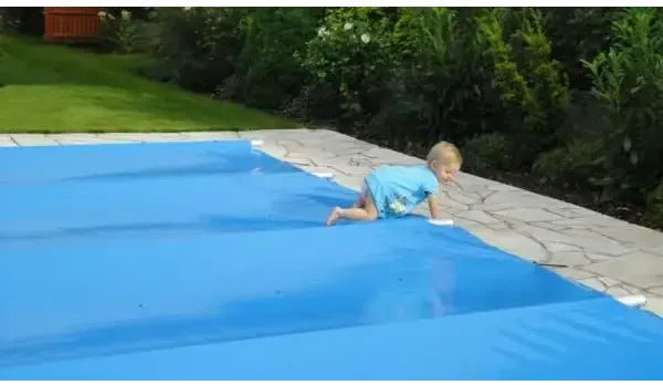 Barn i blå badkläder kryper vid blå pooltäckning inkl handtag för pool inkl handenhet